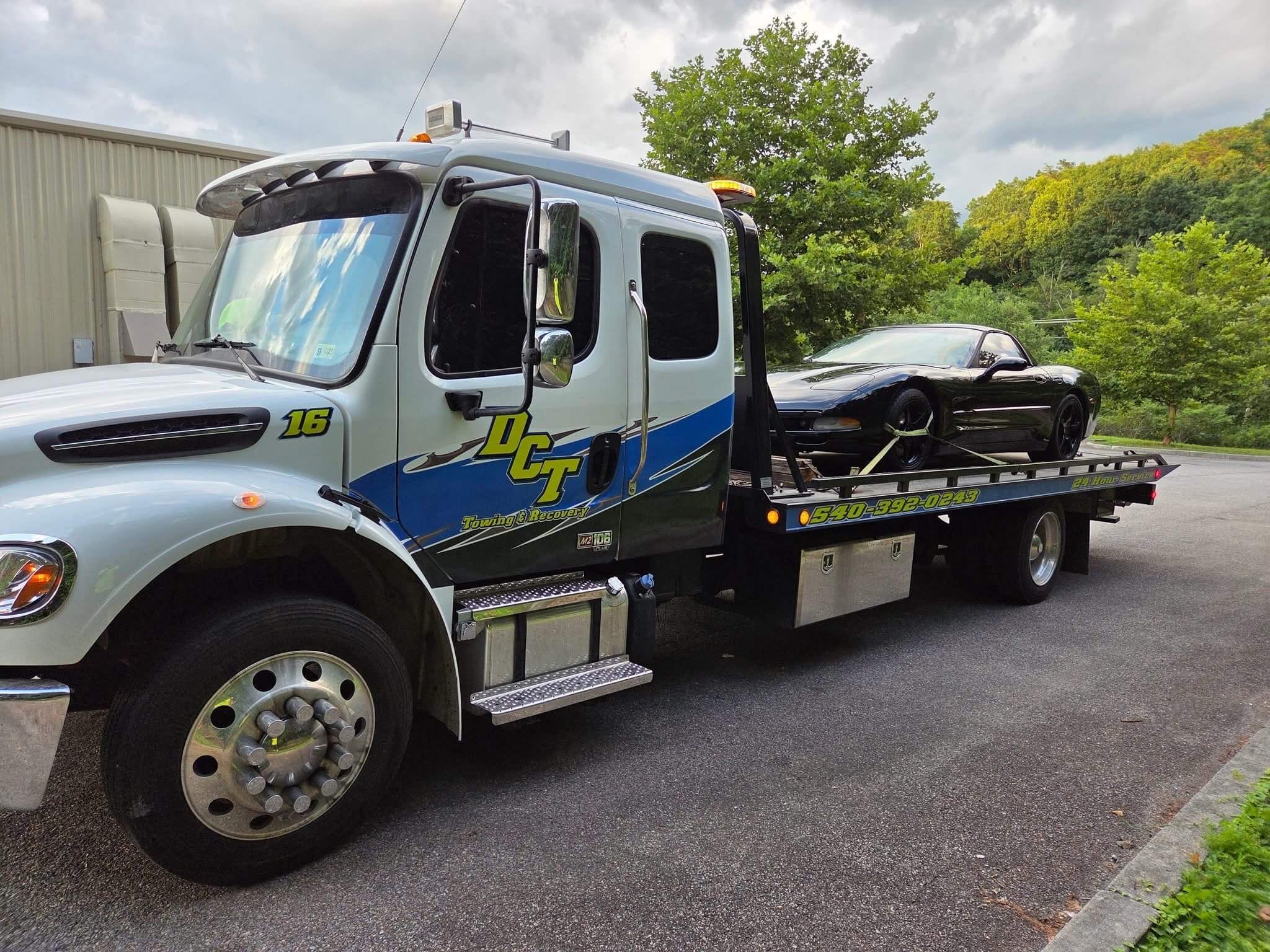 A DCT flatbed carrying a black Corvette secured with wheel straps.