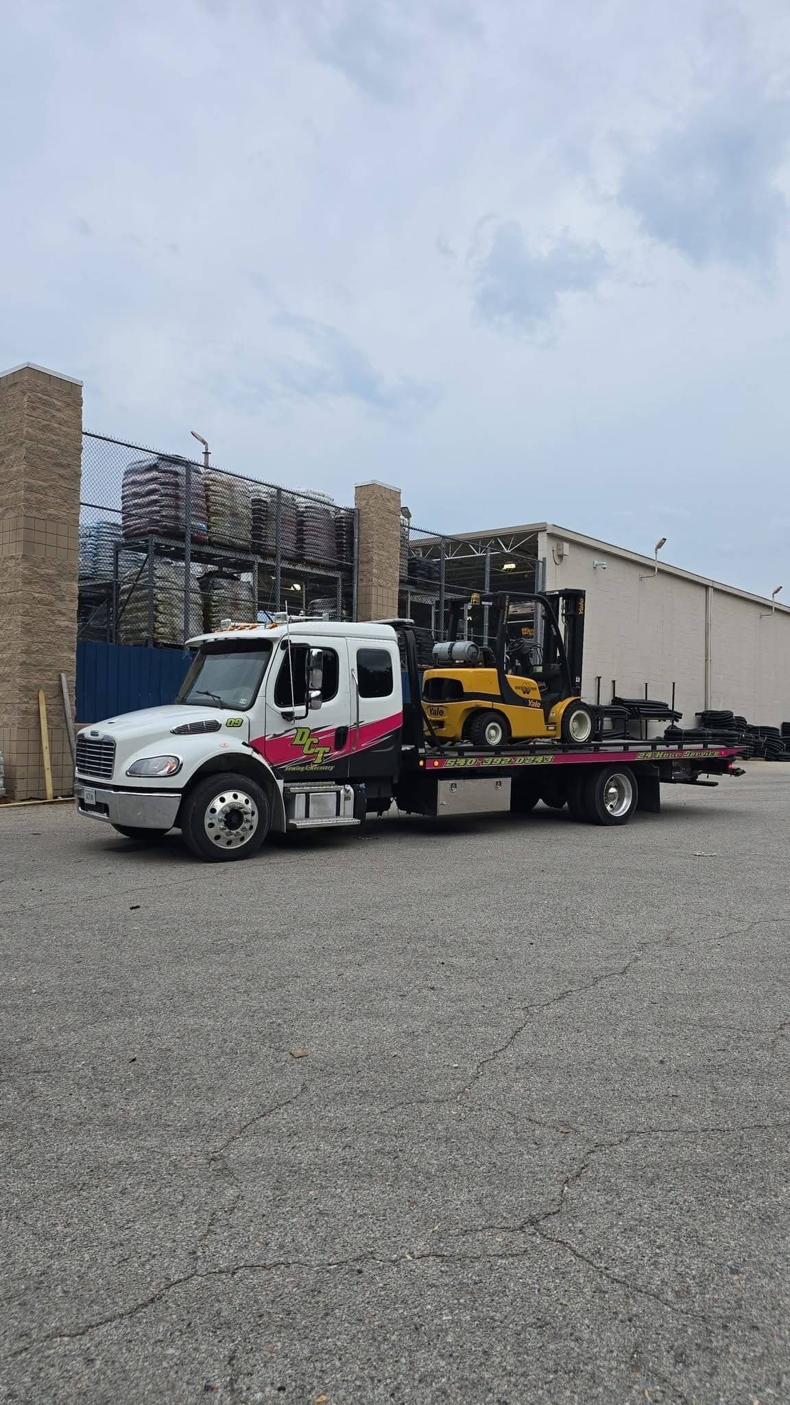 A DCT flatbed loaded with a Yale forklift at a commercial supply yard.