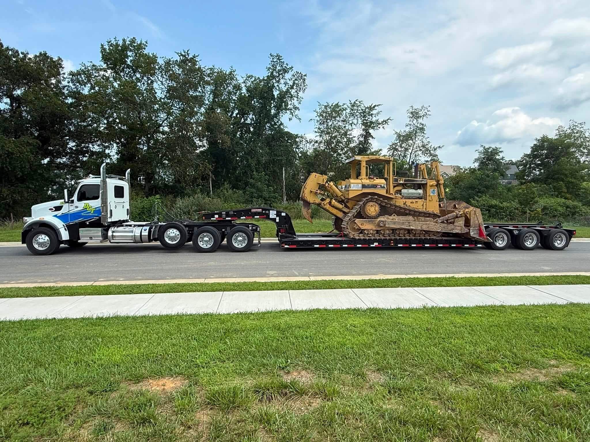 A DCT Peterbilt tractor hauling a CAT bulldozer on a lowboy trailer.
