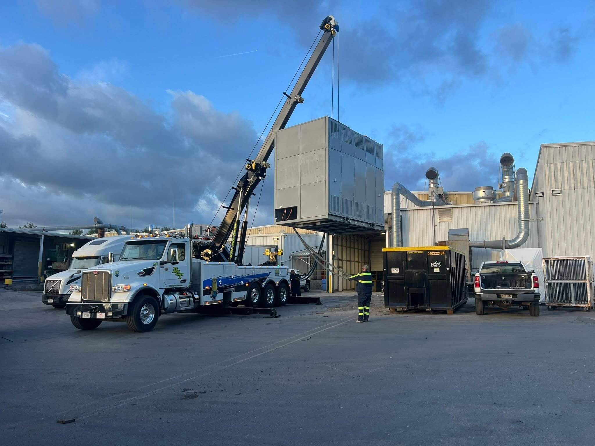 A DCT rotator wrecker lifting a large rooftop HVAC unit at a commercial building.